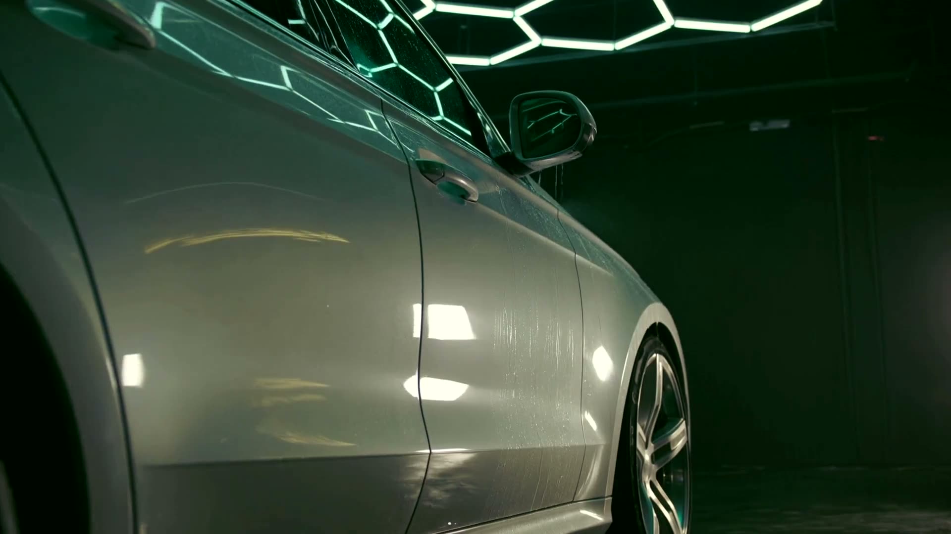 Water beading and sheeting off the freshly sealed flank of a silver car under honeycomb studio lighting.