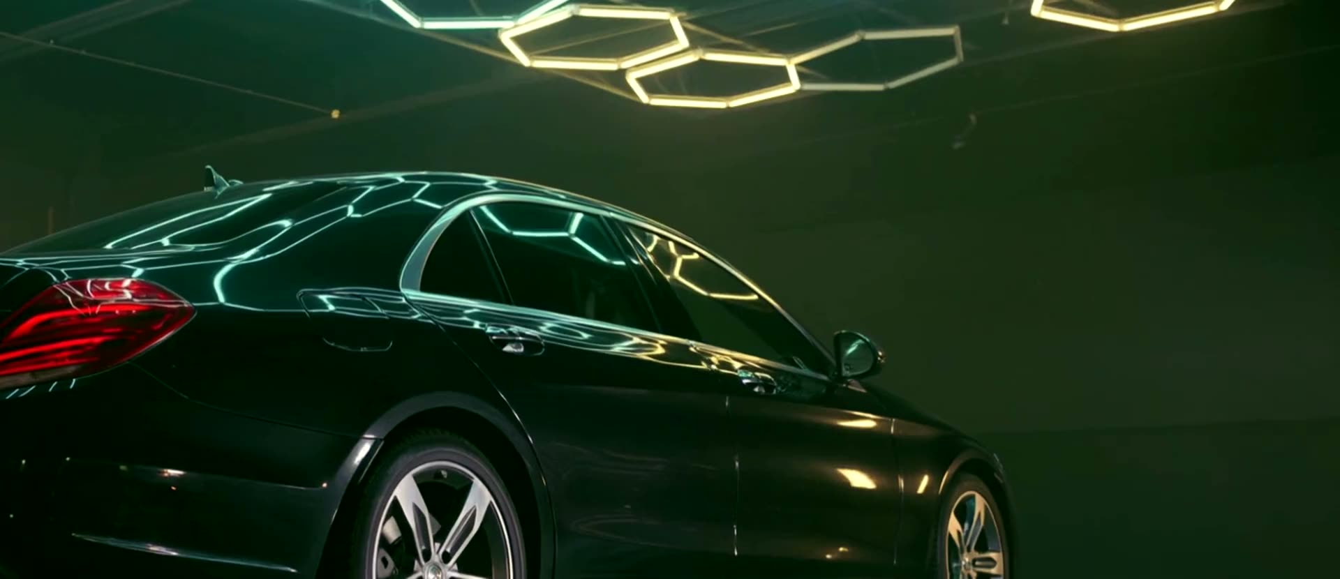 The rear quarter of a freshly detailed black car, honeycomb ceiling lights mirrored across the roof and shoulder line.